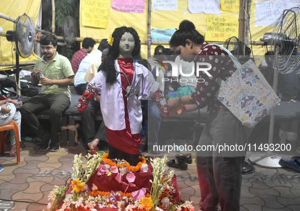 A doctor is tying Rakhis, or a traditional Indian sacred thread, on the wrist of a clay statue of a female doctor depicting a victim of rape...