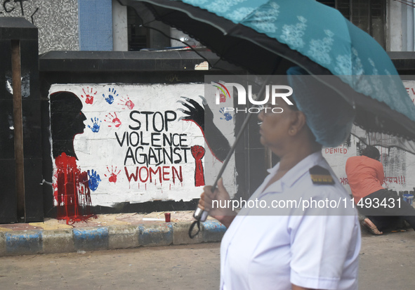 A nurse is passing next to a mural with slogans inside Kolkata Medical College and Hospital campus condemning the rape and murder of a train...