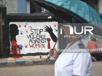 A nurse is passing next to a mural with slogans inside Kolkata Medical College and Hospital campus condemning the rape and murder of a train...