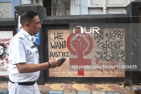 A Kolkata police officer is passing next to a mural with slogans inside Kolkata Medical College and Hospital campus condemning the rape and...