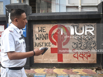 A Kolkata police officer is passing next to a mural with slogans inside Kolkata Medical College and Hospital campus condemning the rape and...