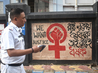 A Kolkata police officer is passing next to a mural with slogans inside Kolkata Medical College and Hospital campus condemning the rape and...