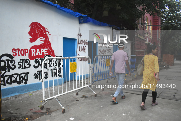 People are passing next to a mural with slogans inside Kolkata Medical College and Hospital campus condemning the rape and murder of a train...