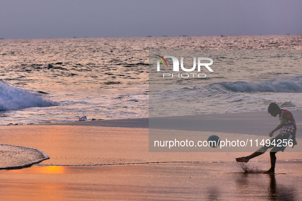 Youth are playing a game of football (soccer) by the ocean at sunset along Paruthiyoor Beach in Paruthiyoor, Kerala, India, on April 15, 202...