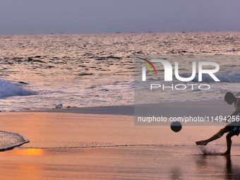 Youth are playing a game of football (soccer) by the ocean at sunset along Paruthiyoor Beach in Paruthiyoor, Kerala, India, on April 15, 202...