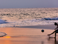 Youth are playing a game of football (soccer) by the ocean at sunset along Paruthiyoor Beach in Paruthiyoor, Kerala, India, on April 15, 202...