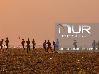 Youth are playing a game of football (soccer) by the ocean at sunset along Paruthiyoor Beach in Paruthiyoor, Kerala, India, on April 15, 202...