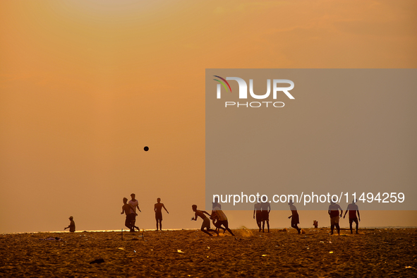 Youth are playing a game of football (soccer) by the ocean at sunset along Paruthiyoor Beach in Paruthiyoor, Kerala, India, on April 15, 202...