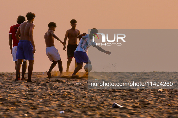 Youth are playing a game of football (soccer) by the ocean at sunset along Paruthiyoor Beach in Paruthiyoor, Kerala, India, on April 15, 202...