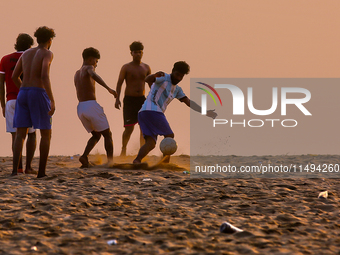 Youth are playing a game of football (soccer) by the ocean at sunset along Paruthiyoor Beach in Paruthiyoor, Kerala, India, on April 15, 202...