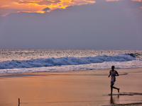 Youth are playing a game of football (soccer) by the ocean at sunset along Paruthiyoor Beach in Paruthiyoor, Kerala, India, on April 15, 202...