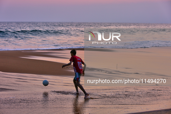 Youth are playing a game of football (soccer) by the ocean at sunset along Paruthiyoor Beach in Paruthiyoor, Kerala, India, on April 15, 202...