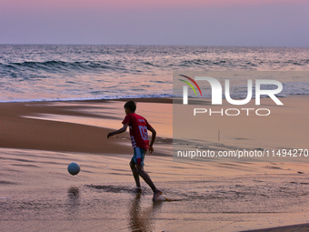 Youth are playing a game of football (soccer) by the ocean at sunset along Paruthiyoor Beach in Paruthiyoor, Kerala, India, on April 15, 202...