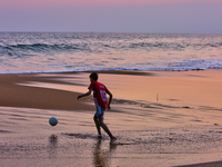 Youth are playing a game of football (soccer) by the ocean at sunset along Paruthiyoor Beach in Paruthiyoor, Kerala, India, on April 15, 202...