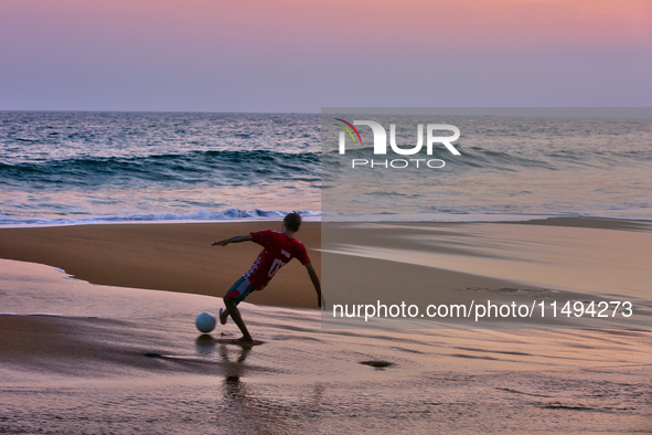 Youth are playing a game of football (soccer) by the ocean at sunset along Paruthiyoor Beach in Paruthiyoor, Kerala, India, on April 15, 202...