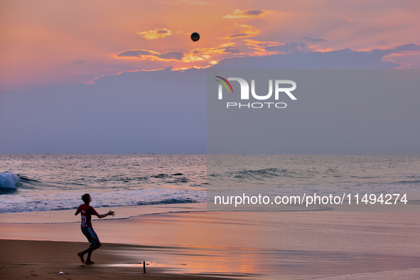 Youth are playing a game of football (soccer) by the ocean at sunset along Paruthiyoor Beach in Paruthiyoor, Kerala, India, on April 15, 202...