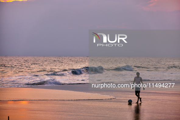 Youth are playing a game of football (soccer) by the ocean at sunset along Paruthiyoor Beach in Paruthiyoor, Kerala, India, on April 15, 202...