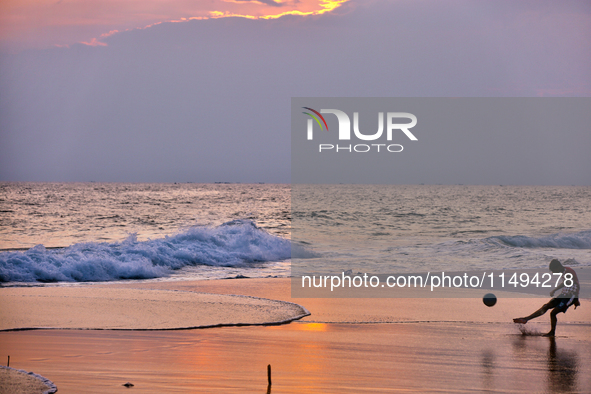 Youth are playing a game of football (soccer) by the ocean at sunset along Paruthiyoor Beach in Paruthiyoor, Kerala, India, on April 15, 202...