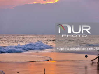 Youth are playing a game of football (soccer) by the ocean at sunset along Paruthiyoor Beach in Paruthiyoor, Kerala, India, on April 15, 202...