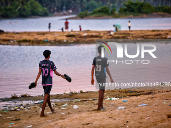 Boys are walking towards a football game as youth are playing a game of football (soccer) by the ocean at sunset along Paruthiyoor Beach in...