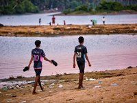 Boys are walking towards a football game as youth are playing a game of football (soccer) by the ocean at sunset along Paruthiyoor Beach in...