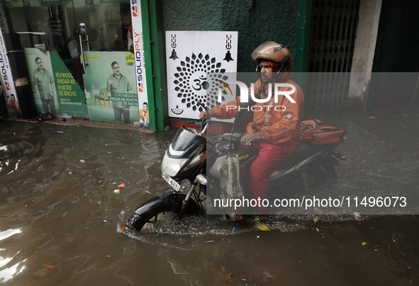 A food delivery person is riding his bike beside a water-logged street after heavy monsoon rain in Kolkata, India, on August 20, 2024. 