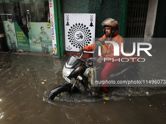 A food delivery person is riding his bike beside a water-logged street after heavy monsoon rain in Kolkata, India, on August 20, 2024. (