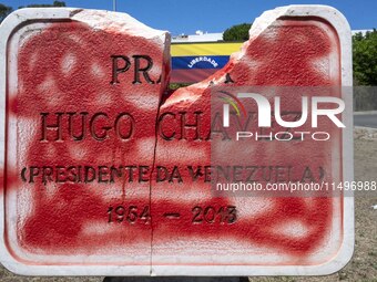 A vandalized stone plate with the words Plaza Hugo Chavez, President of Venezuela, is being seen near a billboard with the Spanish inscripti...