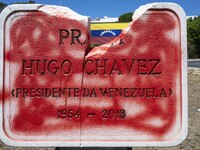 A vandalized stone plate with the words Plaza Hugo Chavez, President of Venezuela, is being seen near a billboard with the Spanish inscripti...