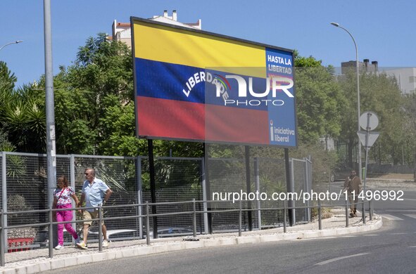 Two people are walking near a billboard with the inscription in Spanish ''Venezuela Libre'' (free Venezuela) in the center of Lisbon, Portug...