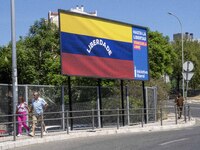 Two people are walking near a billboard with the inscription in Spanish ''Venezuela Libre'' (free Venezuela) in the center of Lisbon, Portug...