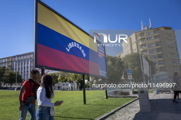 Two people are walking near a billboard with the inscription in Spanish ''Venezuela Libre'' (free Venezuela) in the center of Lisbon, Portug...