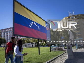 Two people are walking near a billboard with the inscription in Spanish ''Venezuela Libre'' (free Venezuela) in the center of Lisbon, Portug...