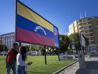 Two people are walking near a billboard with the inscription in Spanish ''Venezuela Libre'' (free Venezuela) in the center of Lisbon, Portug...