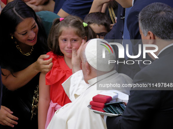 Pope Francis comforts a little girl as she cries at the end of the weekly general audience in The Vatican, on August 21, 2024, at Paul-VI ha...