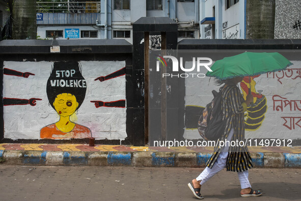 A lady walks past a wall art demanding protest against violence over women and the current crime of rape that has happened at a medical coll...