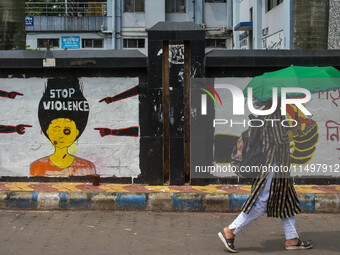 A lady walks past a wall art demanding protest against violence over women and the current crime of rape that has happened at a medical coll...