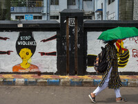 A lady walks past a wall art demanding protest against violence over women and the current crime of rape that has happened at a medical coll...