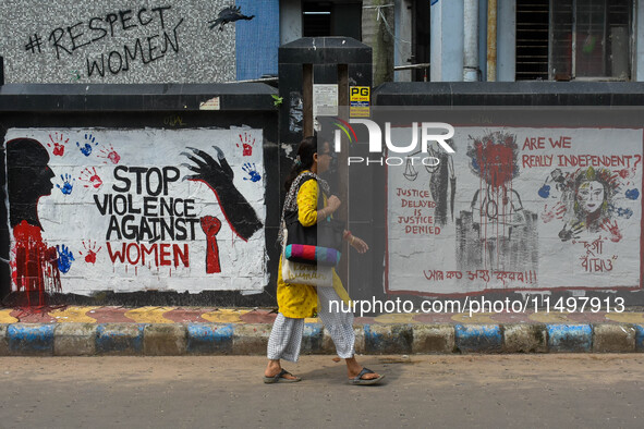 A lady walks past a wall art demanding protest against violence over women and the current crime of rape that has happened at a medical coll...