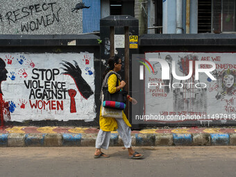 A lady walks past a wall art demanding protest against violence over women and the current crime of rape that has happened at a medical coll...