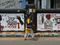 A lady walks past a wall art demanding protest against violence over women and the current crime of rape that has happened at a medical coll...