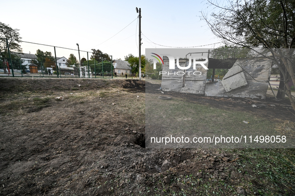 A hole from a Russian artillery shell strike is in the ground near the Levada children's cafe in the central park in Malokaterynivka village...