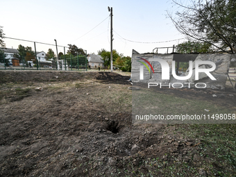 A hole from a Russian artillery shell strike is in the ground near the Levada children's cafe in the central park in Malokaterynivka village...