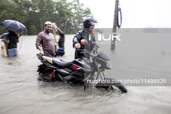 Pedestrians wade through floodwaters up to their waists and knees to safety in the Munsirhat area of Feni district in Chittagong Division, B...