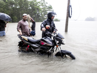 Pedestrians wade through floodwaters up to their waists and knees to safety in the Munsirhat area of Feni district in Chittagong Division, B...