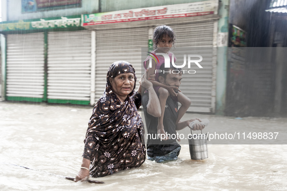 Pedestrians wade through floodwaters up to their waists and knees to safety in the Munsirhat area of Feni district in Chittagong Division, B...