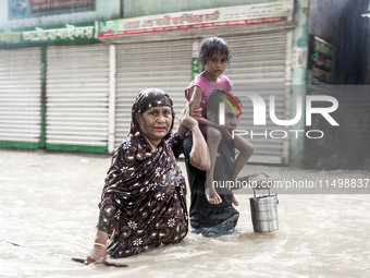 Pedestrians wade through floodwaters up to their waists and knees to safety in the Munsirhat area of Feni district in Chittagong Division, B...