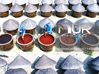 Workers use a wooden rake to turn sauces at the old soy sauce natural drying sauce shop in Yanhe Village, Rucheng Street, Rugao city, East C...