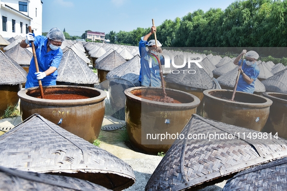 Workers use a wooden rake to turn sauces at the old soy sauce natural drying sauce shop in Yanhe Village, Rucheng Street, Rugao city, East C...