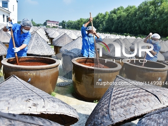 Workers use a wooden rake to turn sauces at the old soy sauce natural drying sauce shop in Yanhe Village, Rucheng Street, Rugao city, East C...